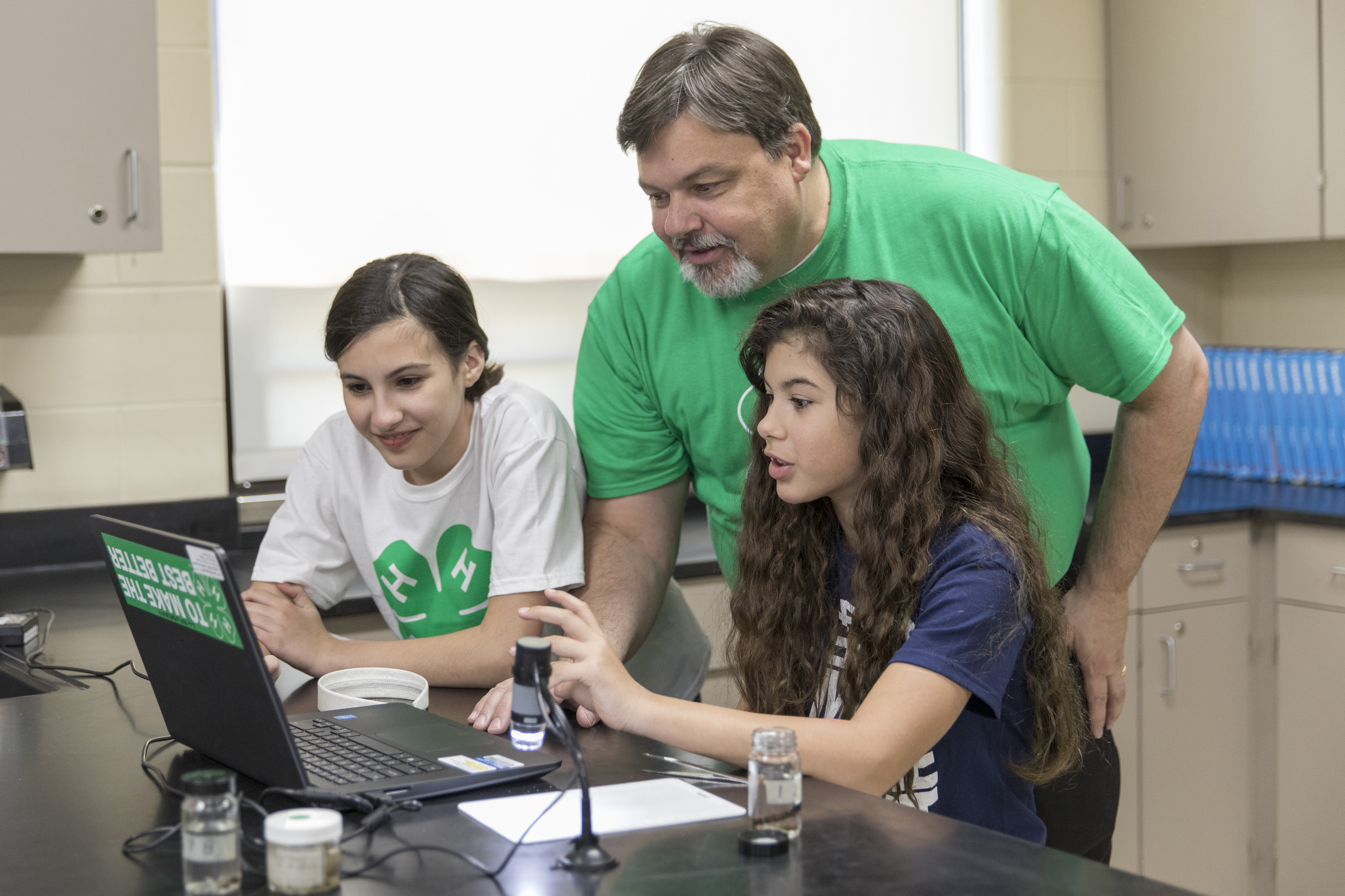 Volunteer assists members on a computer A male volunteer assists two 4-H members on a computer.