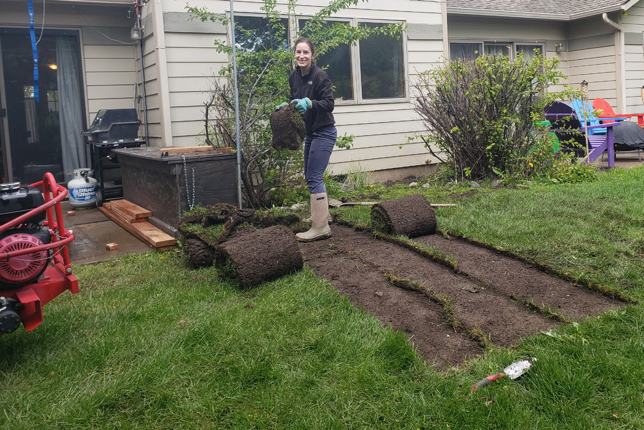 Woman neatly cutting out rows of grass and rolling it up.