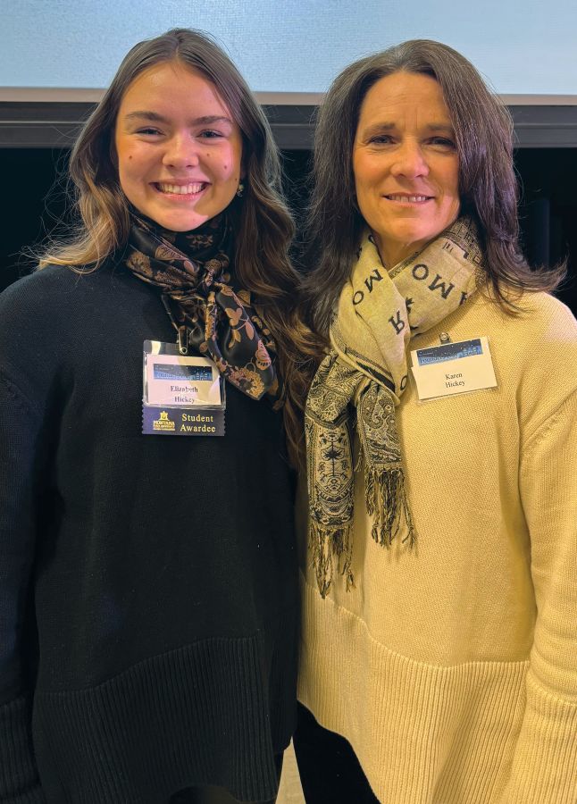 Two women, a mother and daughter, smile at the camera with their arms around each other's back. They are both wearing name badges.