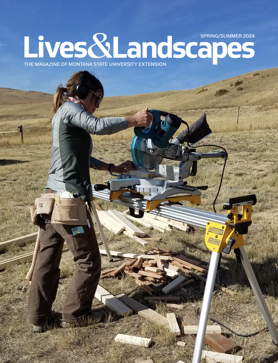 A woman wearing safety gear and a toolbelt cuts a piece of lumber with a table saw set up outdoors.