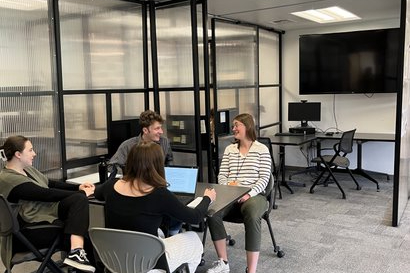 Four writers sit around a table in the Wilson Writing Center, with laptops in front of them. They are excitedly discussing something.
