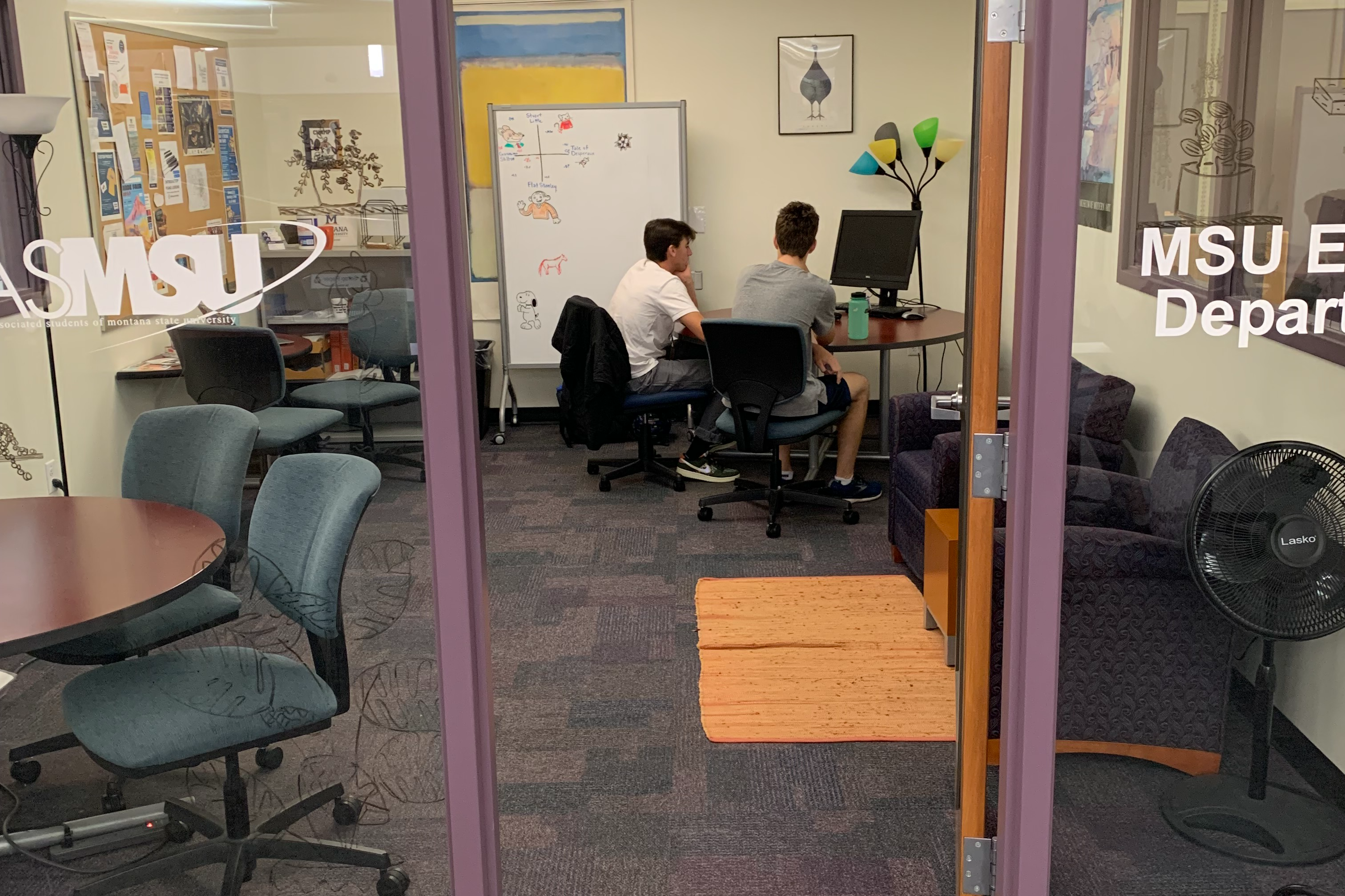 A view of a tutor and writer working together at a table in the Library Writing Center, as seen from the outside.